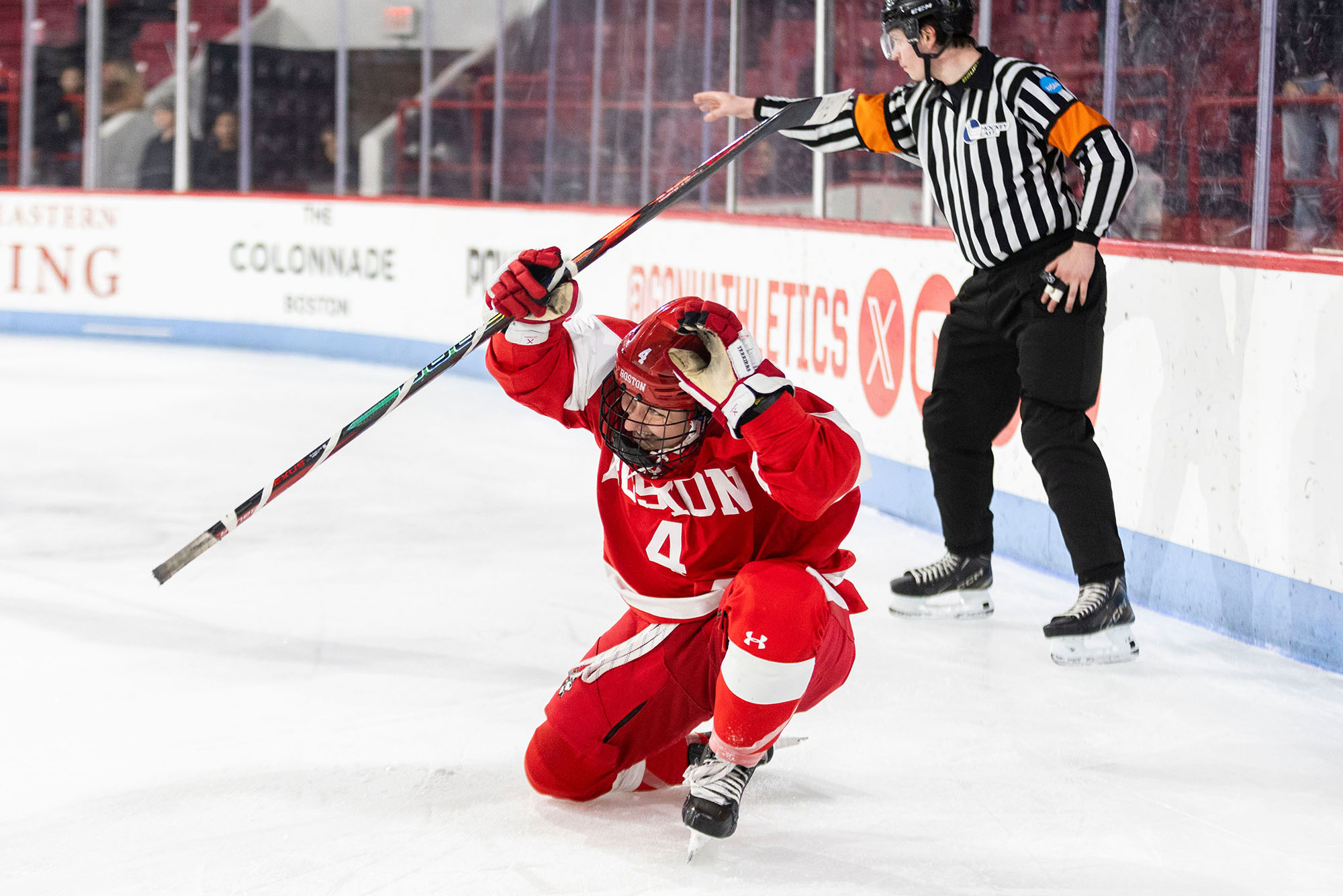 Photo: BU Women's Hockey player #4 crouched and smiling on the ice with her stick raised in the air