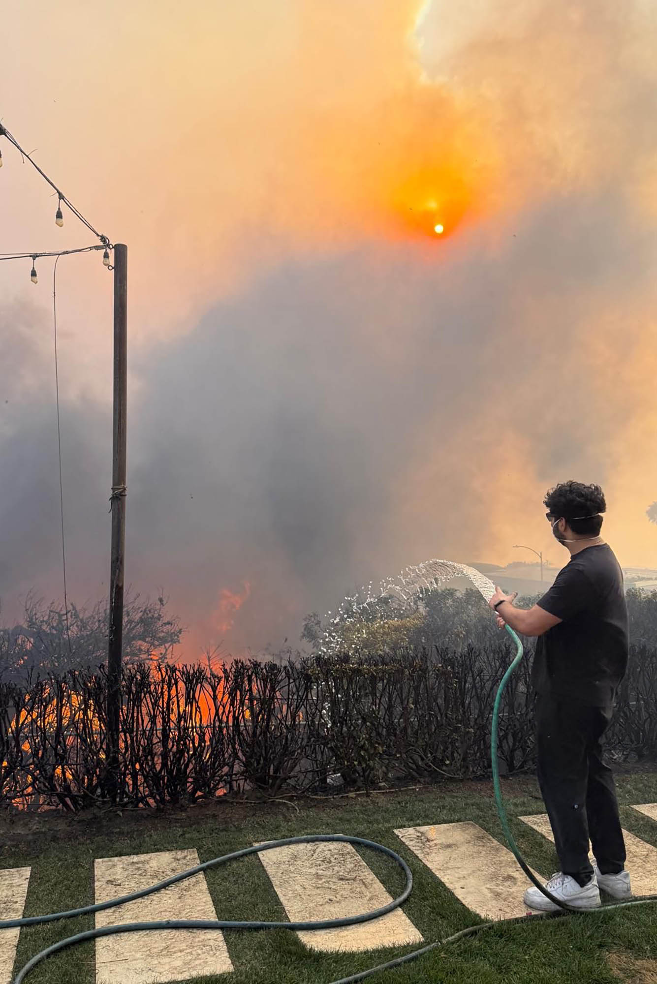 Photo: A person with a hose attempts to snuff out a steady fire in a bush.