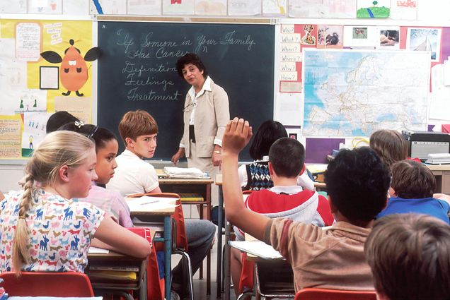 Photo: A stock photo of a classroom full with children, a lone child in the center raising his hand.