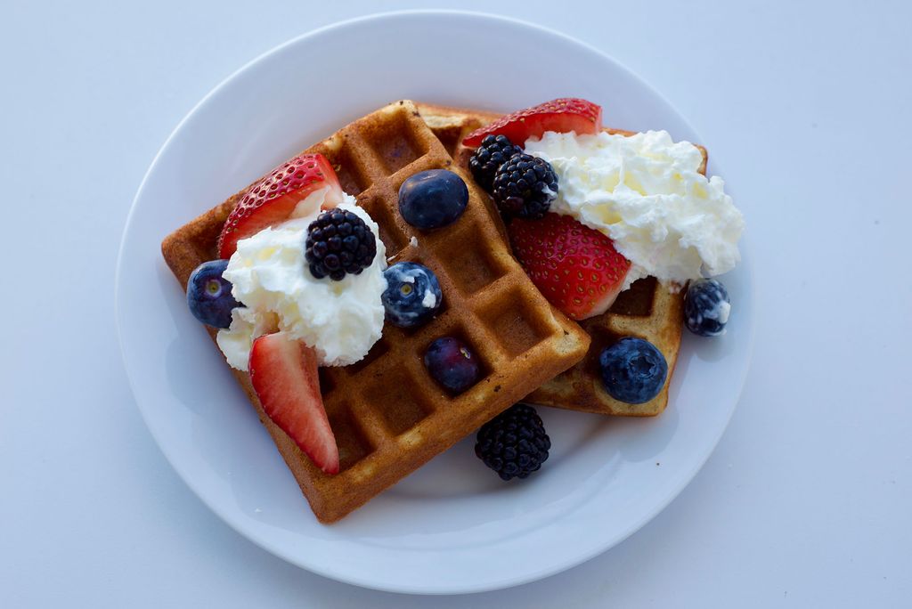 Photo: A waffle on a white plate with whipped cream, strawberries, and blueberries on top