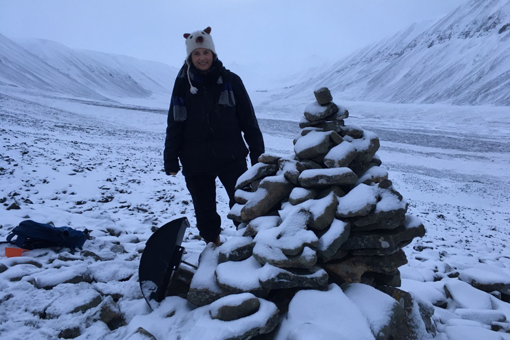 Photo: Adriana Craciun, a BU professor, standing next to a pile of snowy rocks while wearing winter gear and a hat with an animal face on it