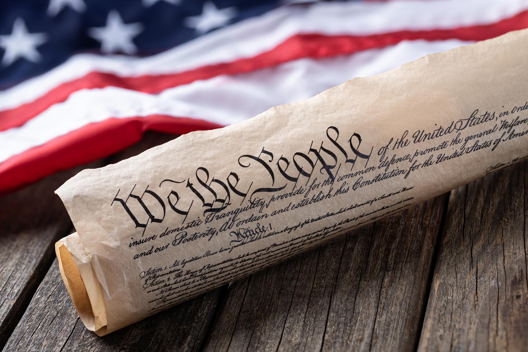 Photo: United States constitution with American flag in background on rustic wooden table