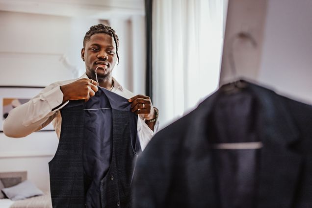 Photo: Young black man putting on a black formal vest