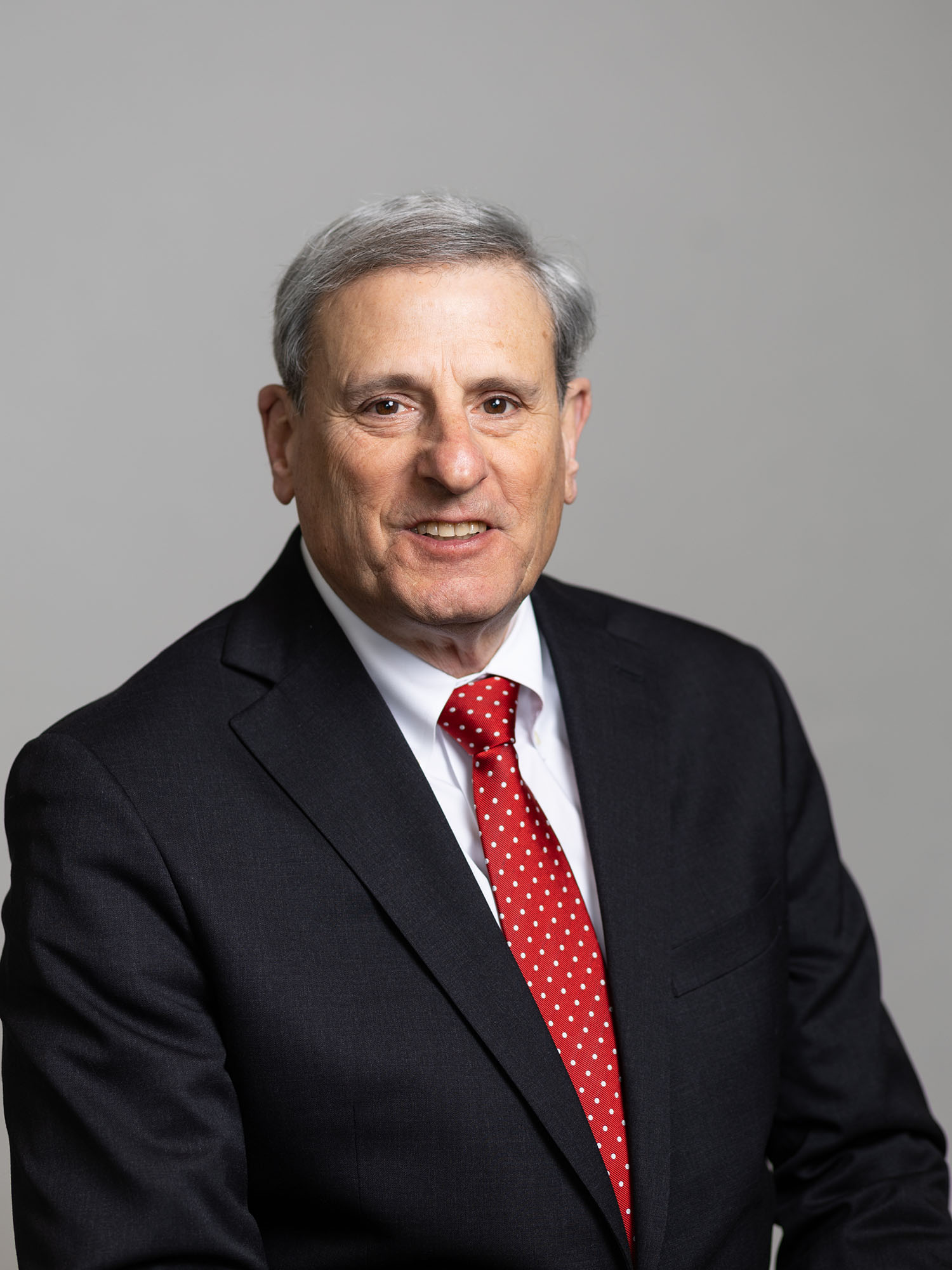 Photo: A man smiling for a portrait while wearing a dark suit and vibrant red tie