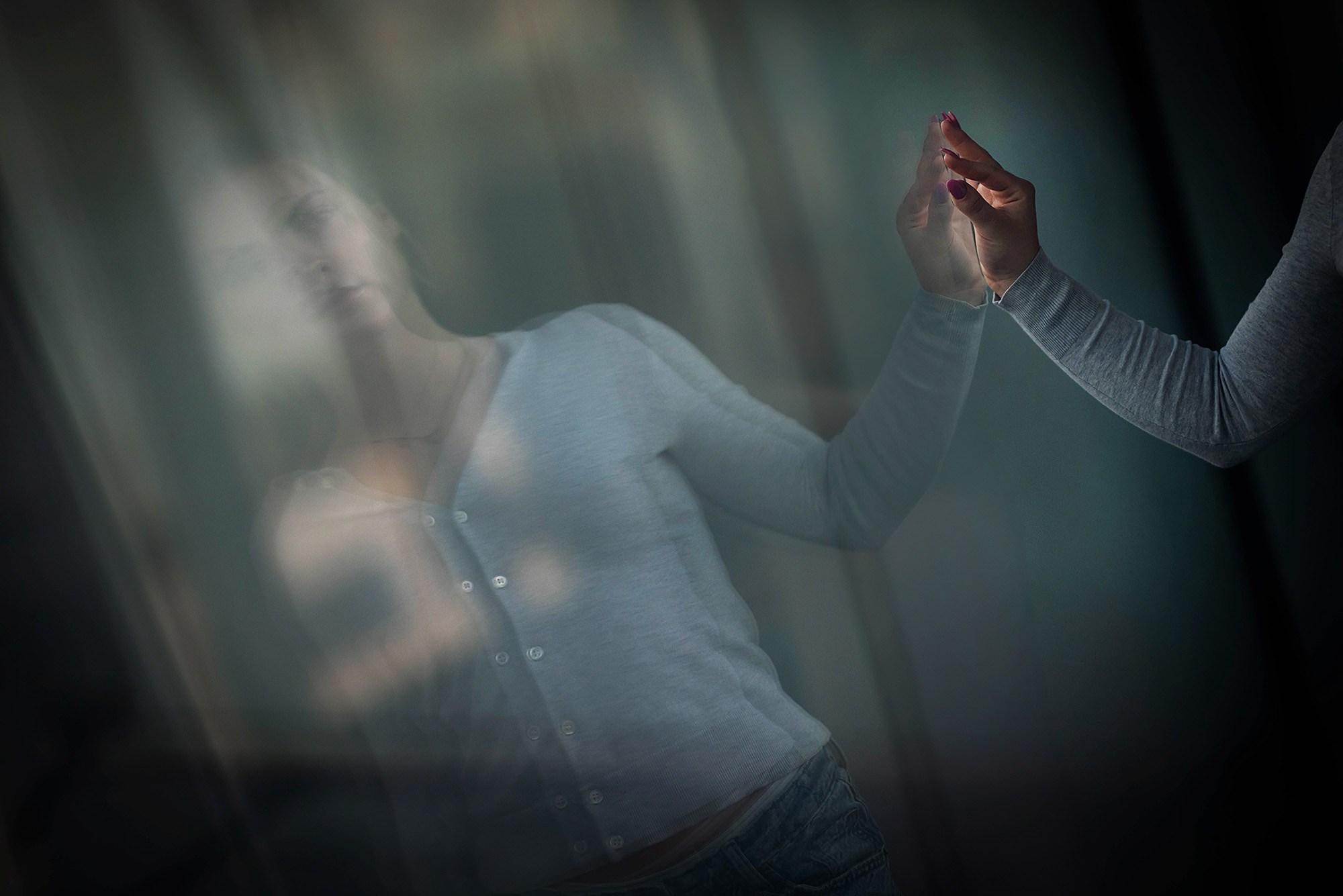 Photo: A blonde female student wearing a gray cardigan looking at her reflection with an arm extended