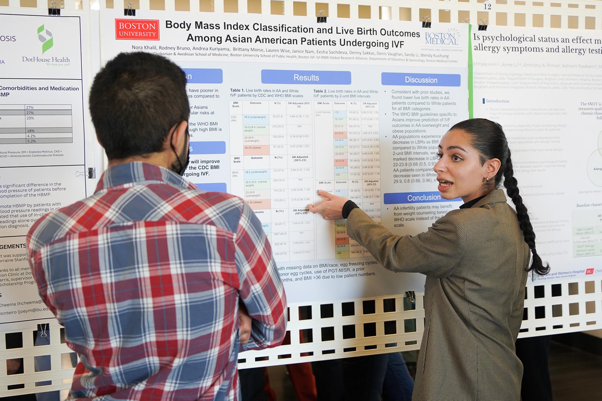 Photo: Two individuals look at a chart. The one on the right, a women with a long braid and a blazer, looks to the man on the left as she explains the chart.