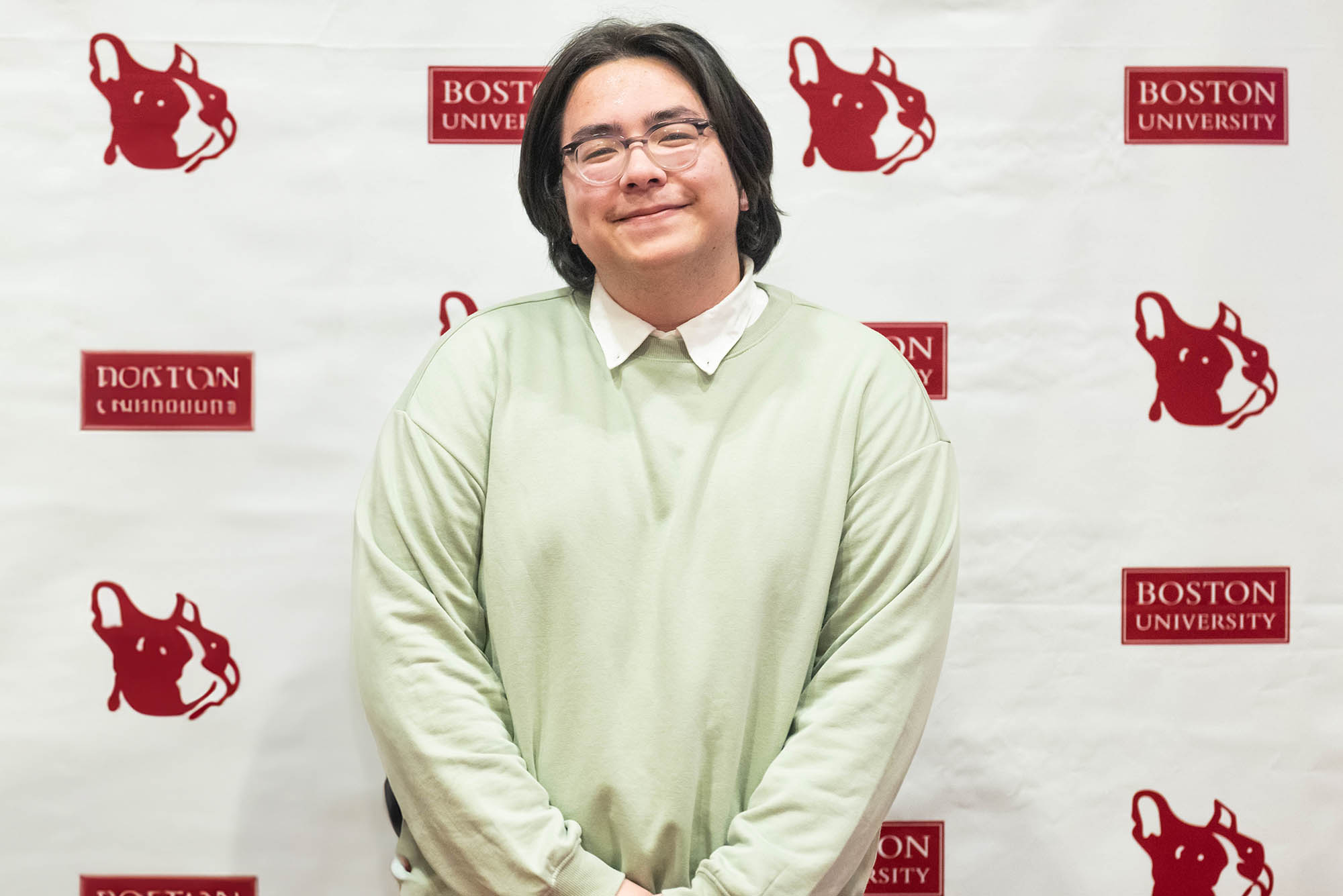 Photo: A young man with chin length black hair poses for a photo in a green sweater.