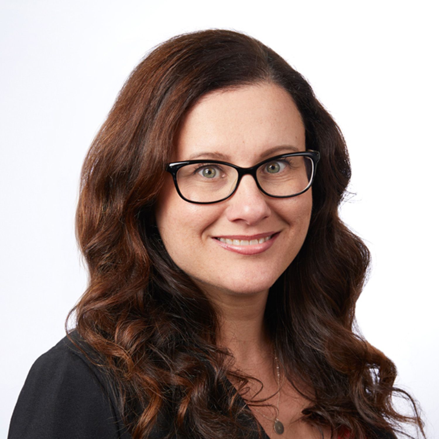 Photo: A woman with reddish-brown hair and glasses smiling and posing for a headshot