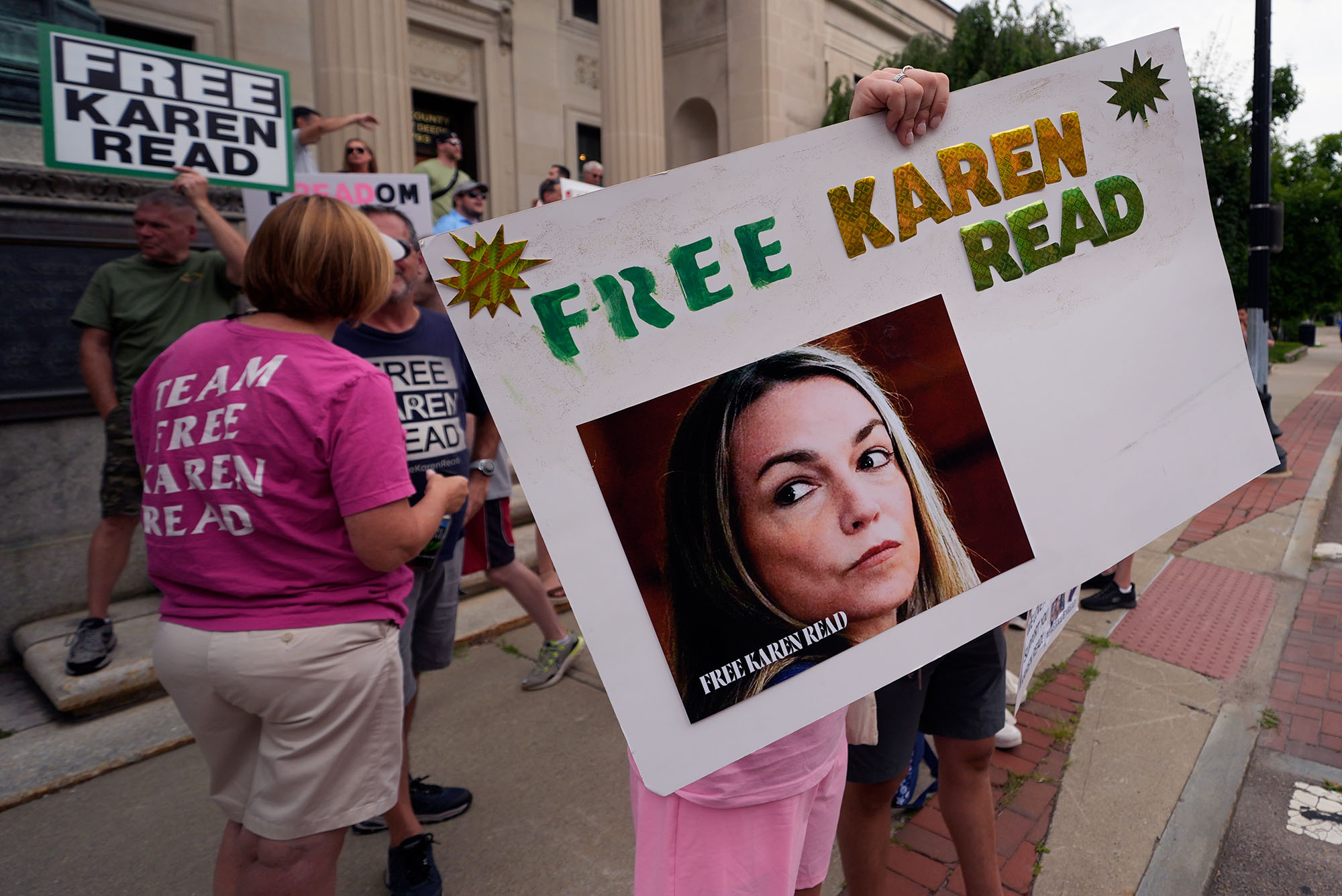 Photo: A group of people holding signs in support of Karen Read. Prominent poster says "Free Karen Read" with a picture of a white woman