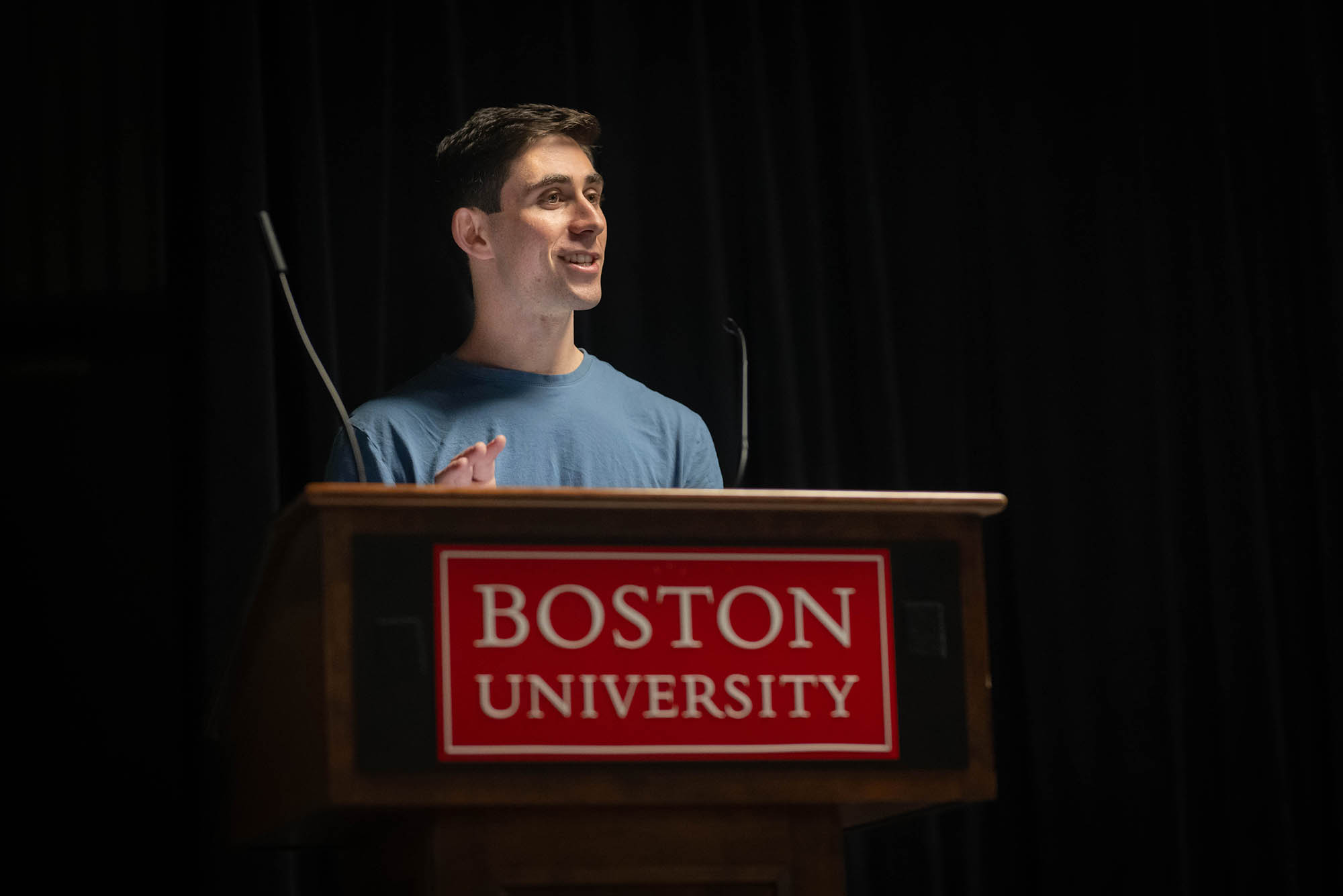 Photo: A white man with short brown hair and a dusty blue shirt on a podium.