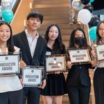 Photo: A group of students in formal attire smile for a photo, each with a certificate of their win.