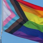 Photo: A picture of a pride flag being raised in front of a blue sky
