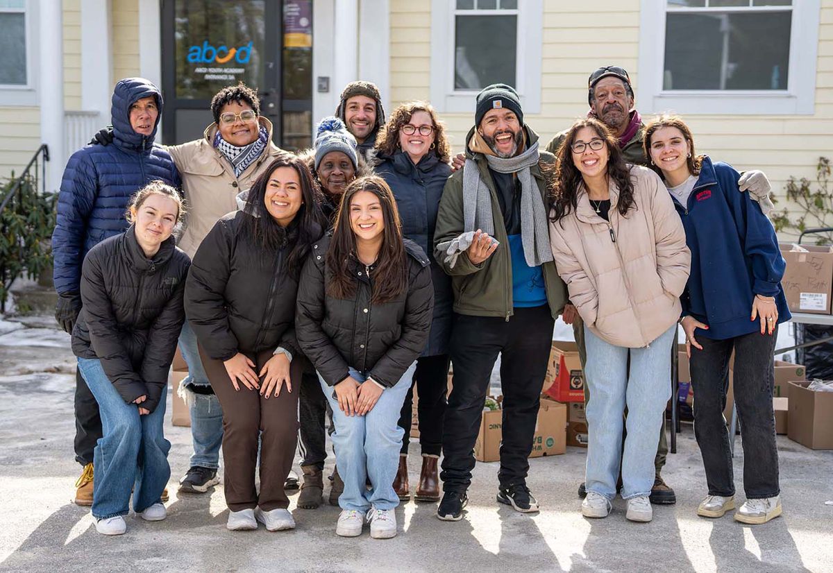 Photo: A group of people smiling and posing while wearing winter jackets outside of a building