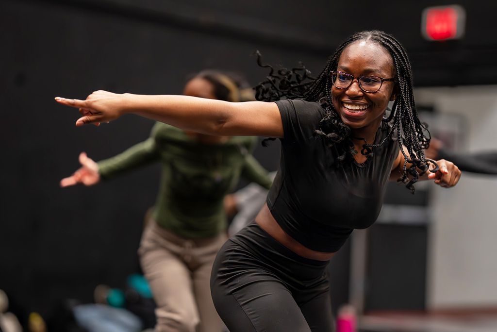 Photo: A woman in the foreground dancing with a few other people in the background. Her arm is extended and she is smiling