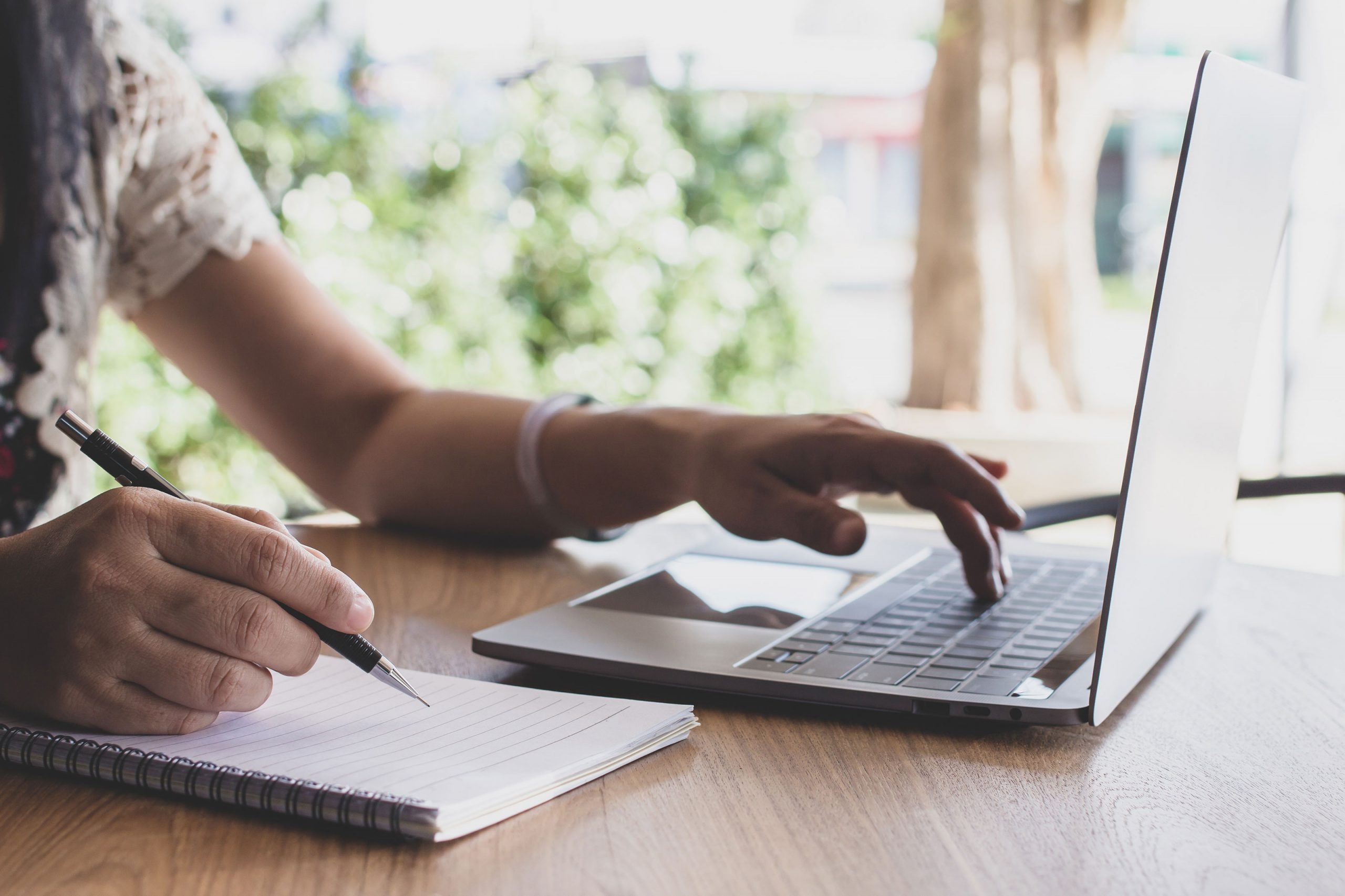 Woman writing in notebook and working on laptop computer