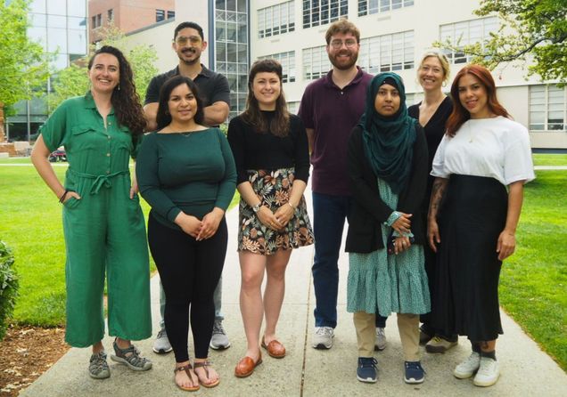 Eight people smile on a green campus quad