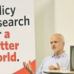 Brett Christophers beside a sign reading "Policy research for a better world"
