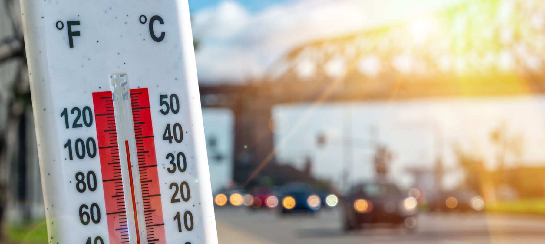 Thermometer reading 100 degrees fahrenheit with highway and cars in background.