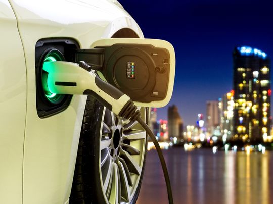 Electric vehicle charger with city skyline at night.
