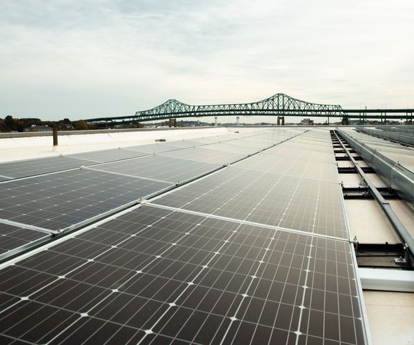 Rooftop solar panels on top of a building with the Tobin Bridge and Charlestown, MA, United States in the background.