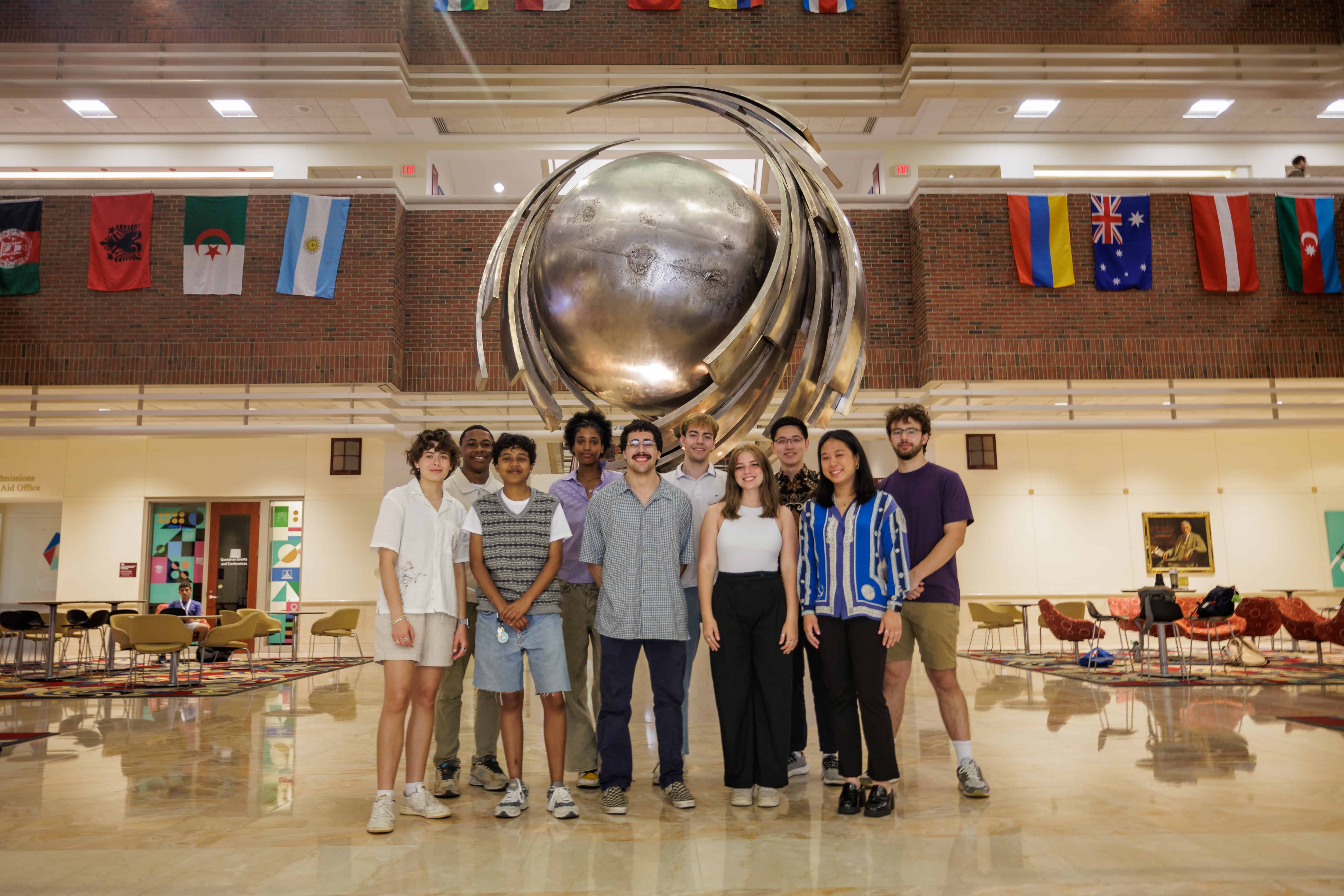 Cohort of students posed in front of a large metal statue in a building atrium