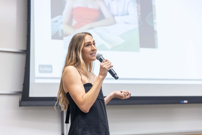 Woman presenting her venture on stage speaking into a microphone