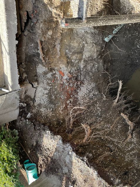 A large work site hole in front of a building with tree routes protruding into the hole.