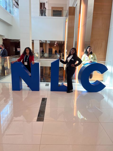 Gloria poses with 2 colleges in front of NLC signs