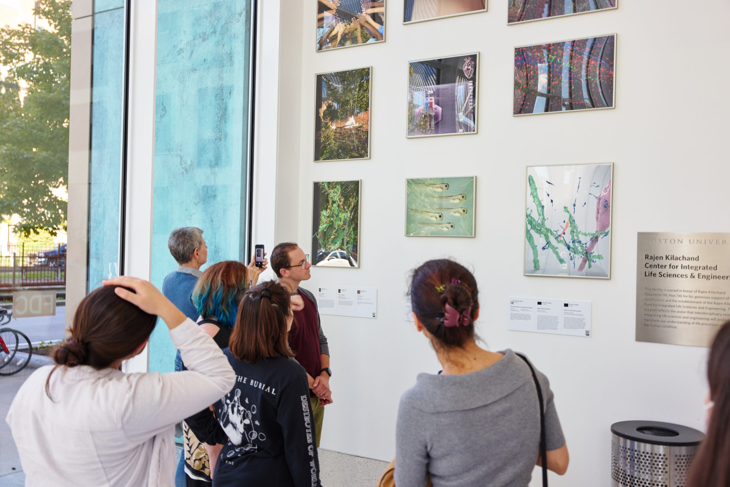 People looking at frame photos hanging on a wall