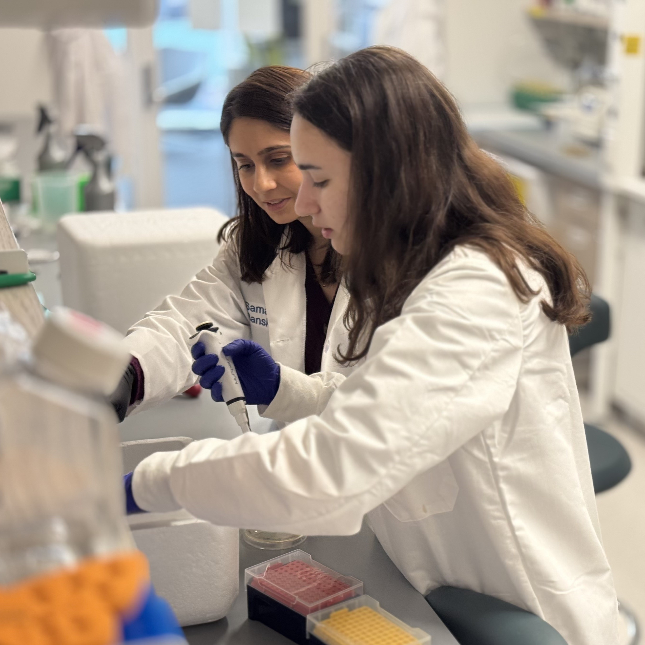 two people in lab coats pipetting in a wet lab
