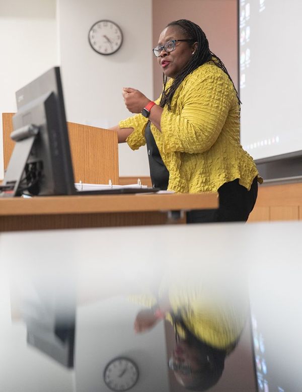 Dean Onwuachi-Willig lectures from the podium with computer screen in front.