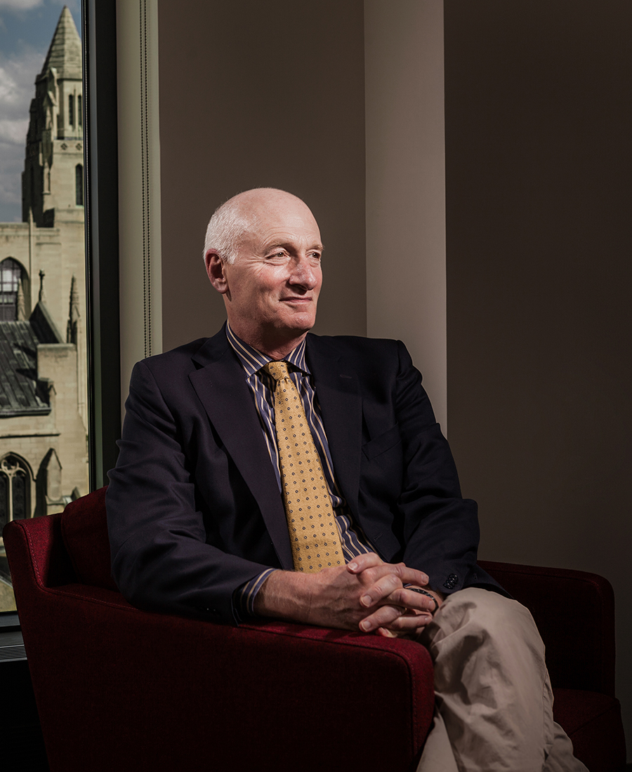 Professor Robert Volk sits in a red chair with the BU School of Theology in the background