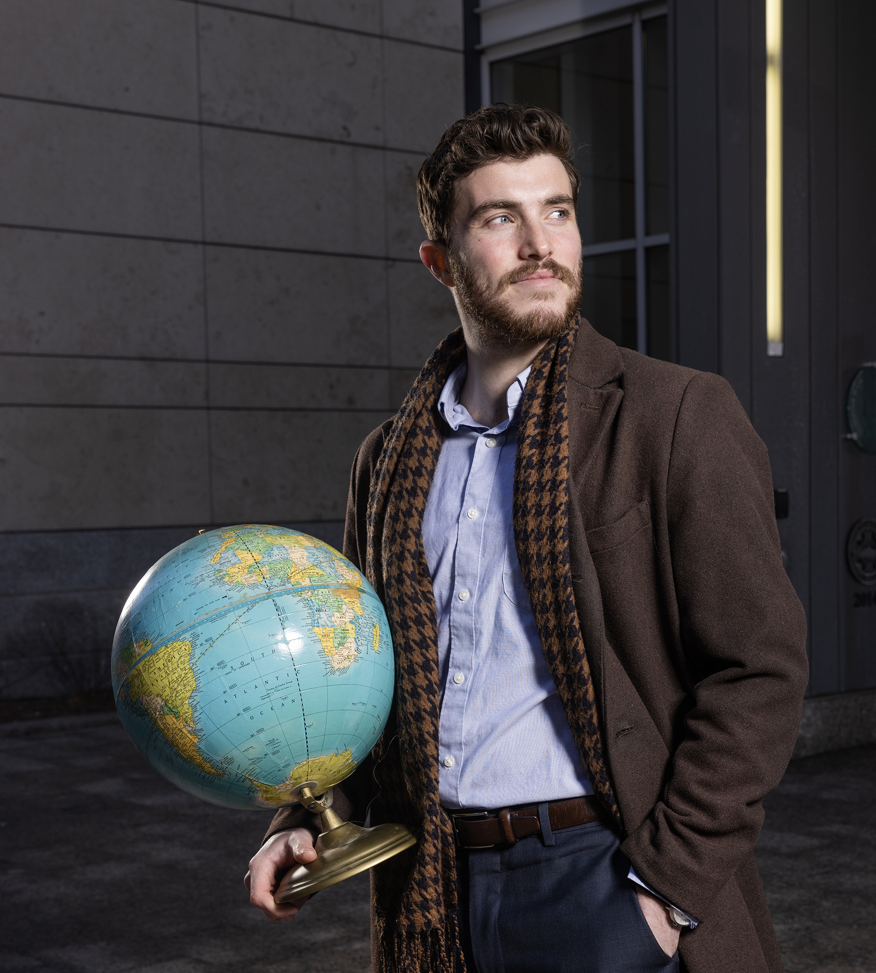 Sam Banker, Class of 2023, stands outside the Redstone building holding a globe