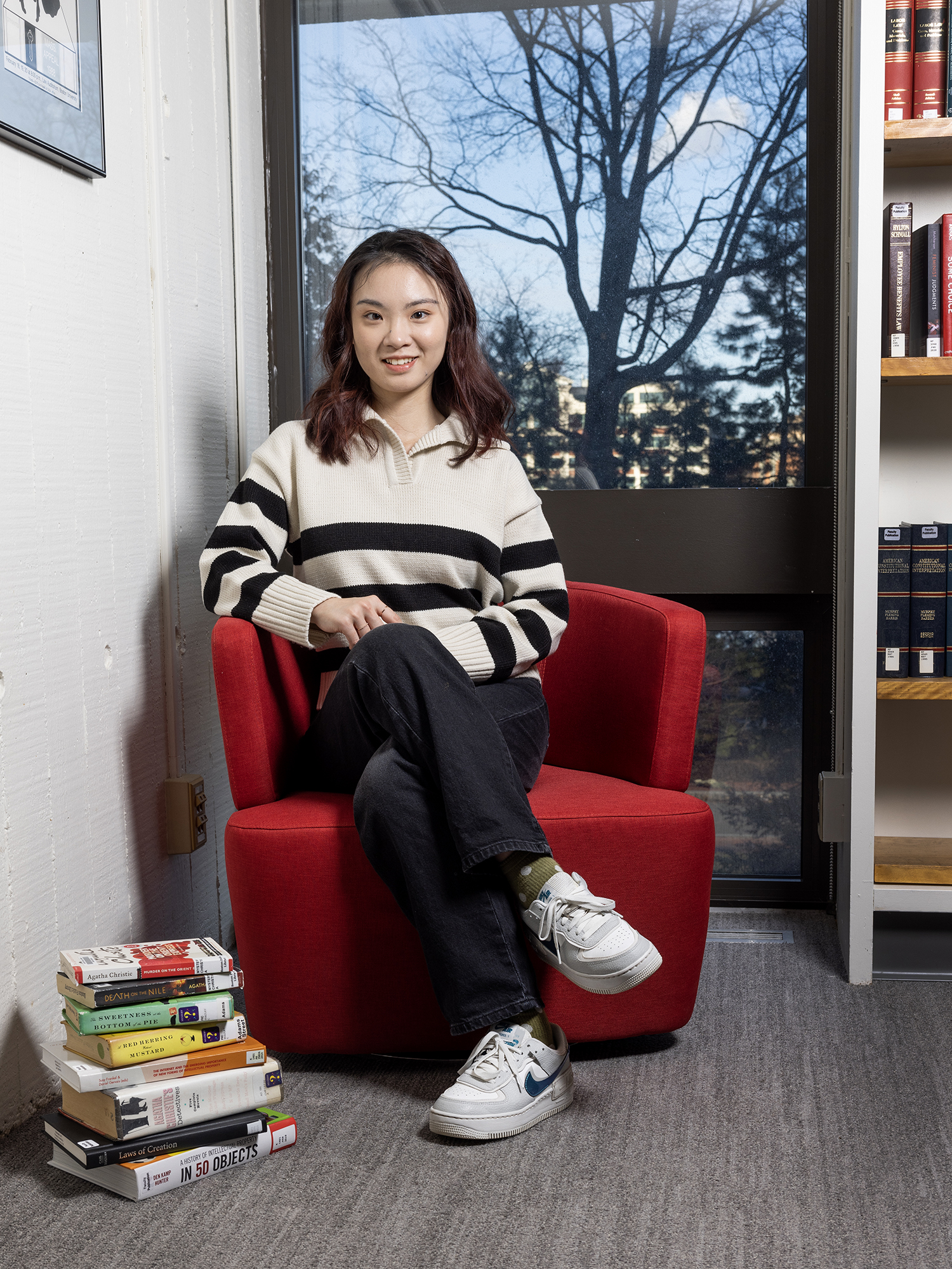 Zhuoming Yuan, LLM Class of 2023, sits in a red chair with books stacked next to her