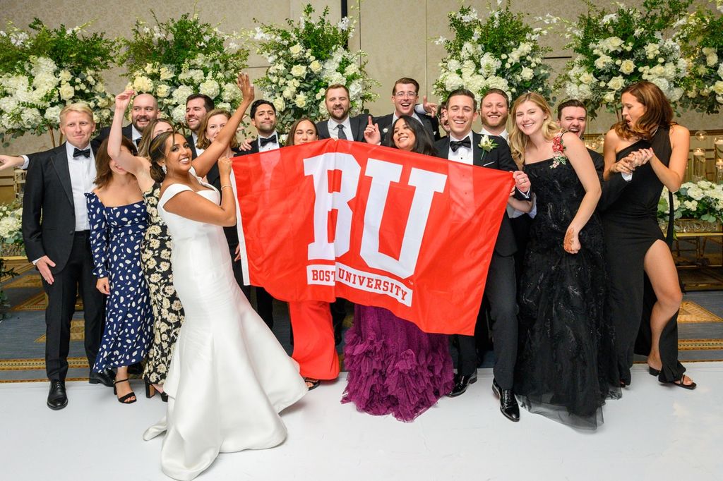 A large group of BU Law alumni at a wedding. The bride and friends hold up a red banner with Boston University School of Law in white text.