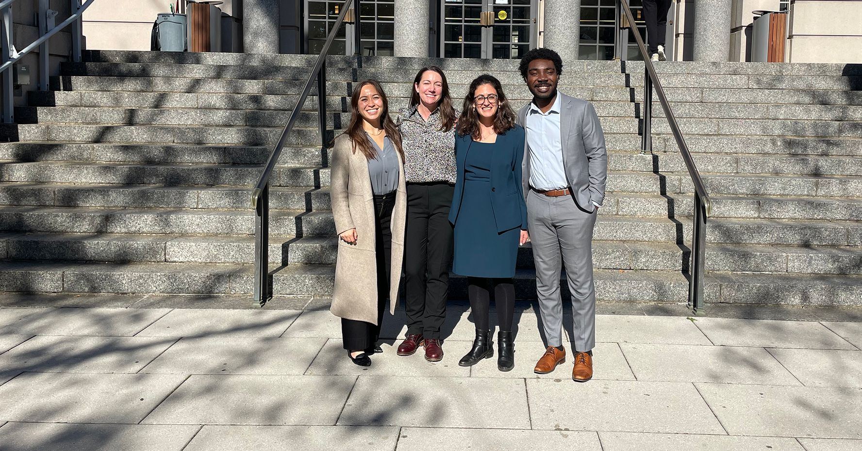 Four people in business attire stand on the steps of a court building in Boston, Massachusetts.