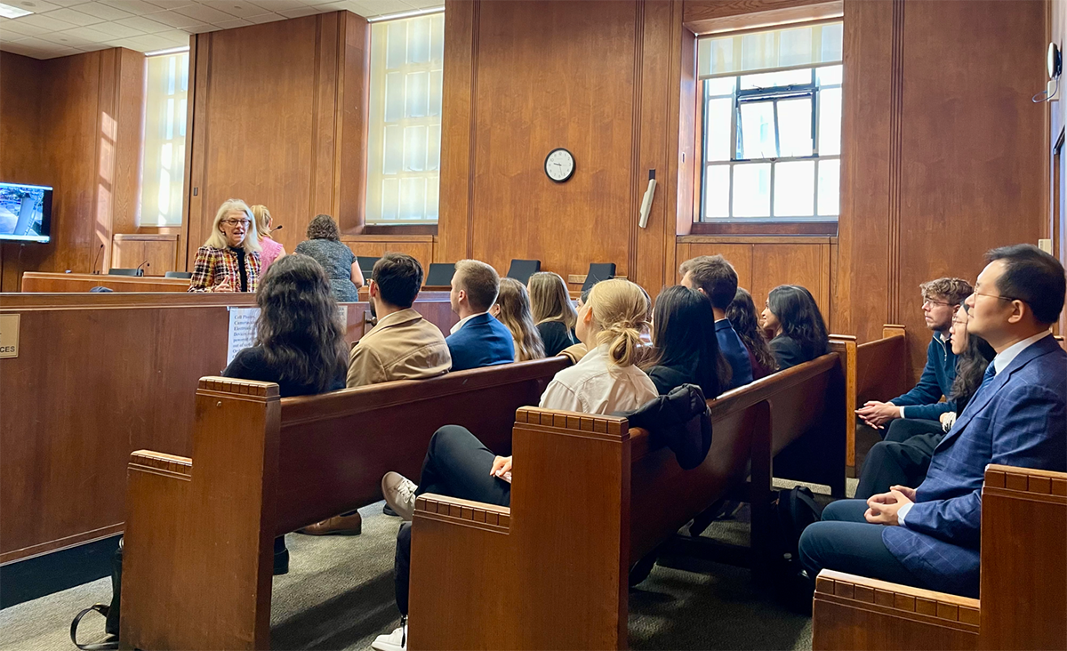 A dozen law students sit in a courtroom listening to a professor speak.