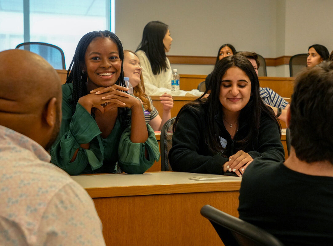 Two female students chat with their classmates in a lecture hall.