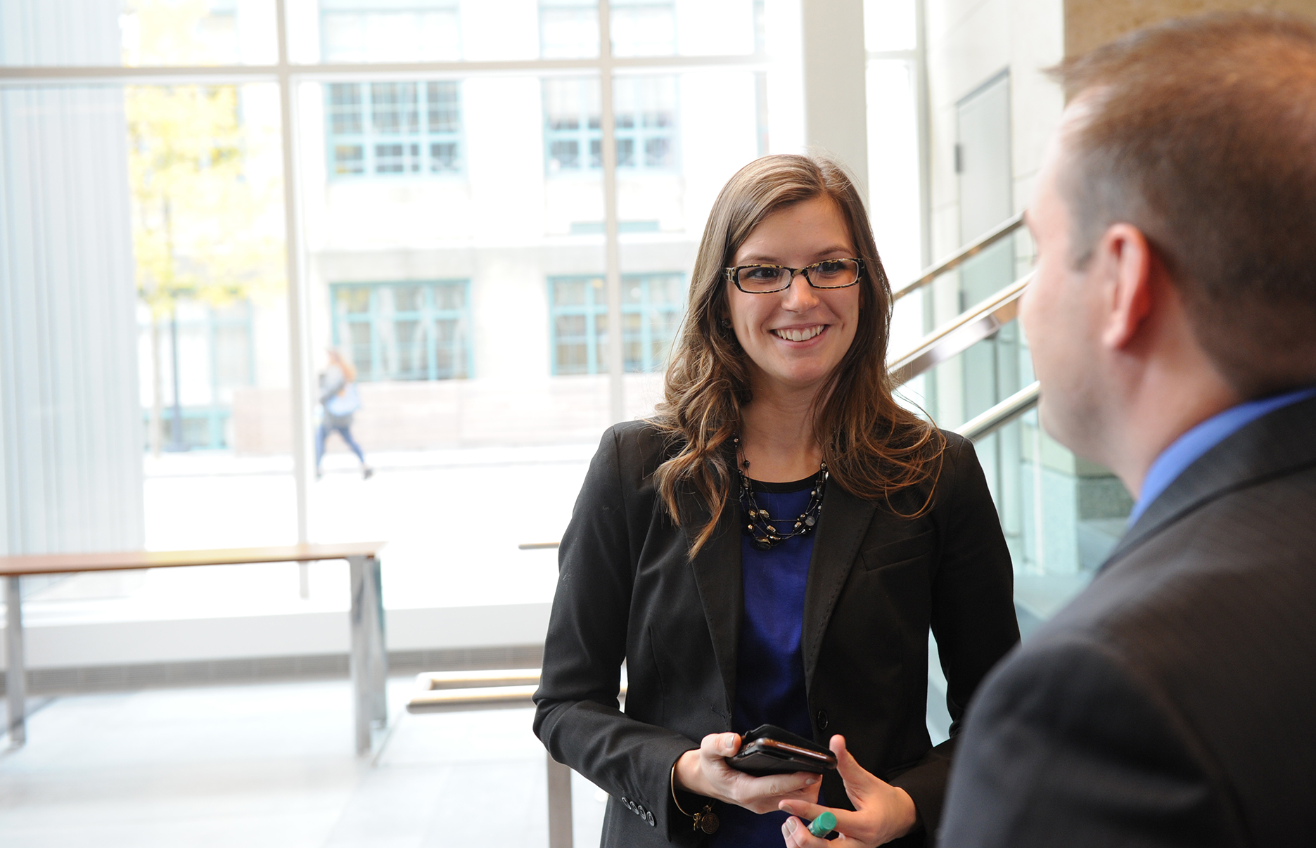 Two students in business attire converse in the atrium.