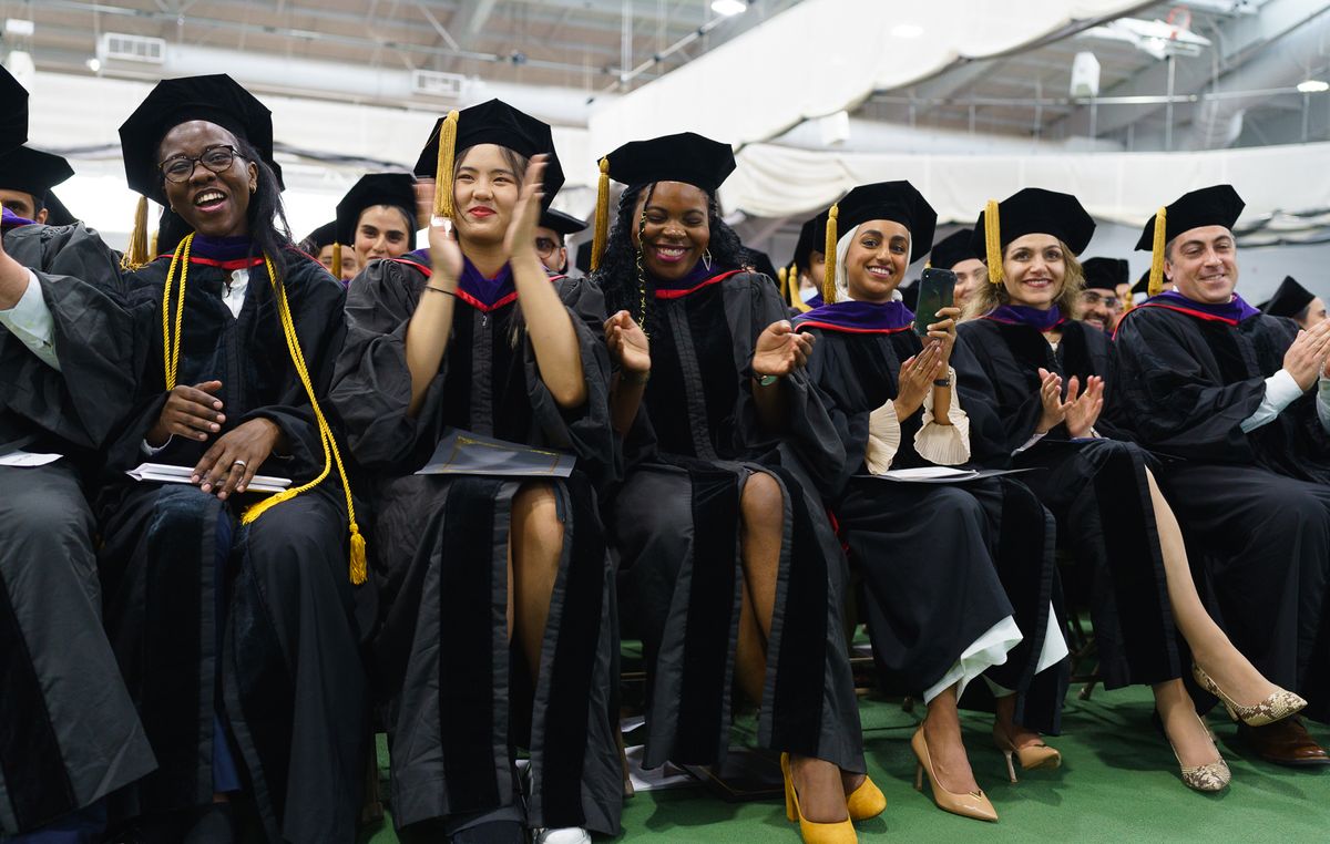 A diverse group of JD students clap at Commencement.