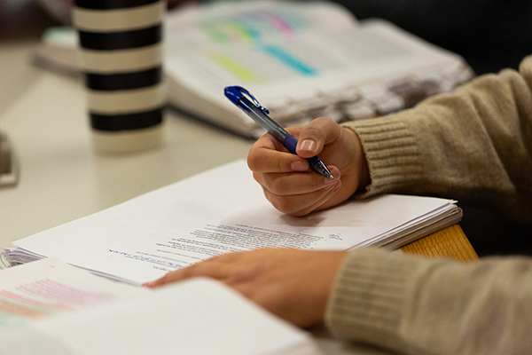 A student reads in a lecture hall. Only their hands are pictured.