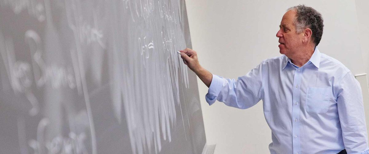Associate Professor of the Practice Hal Tepfer writes equations on a chalkboard in an Actuarial Science classroom