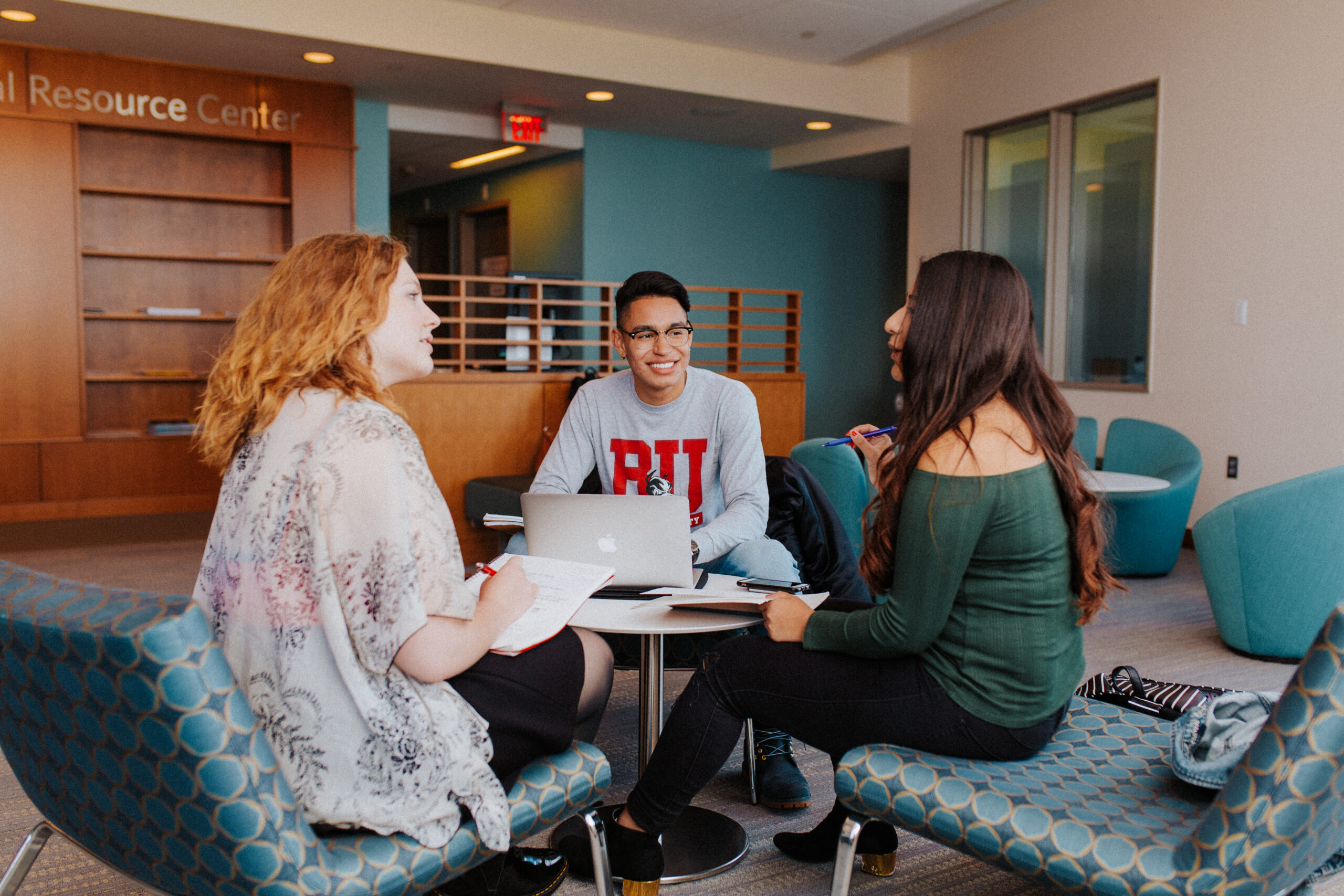 Three students sitting at a round table working and smiling.