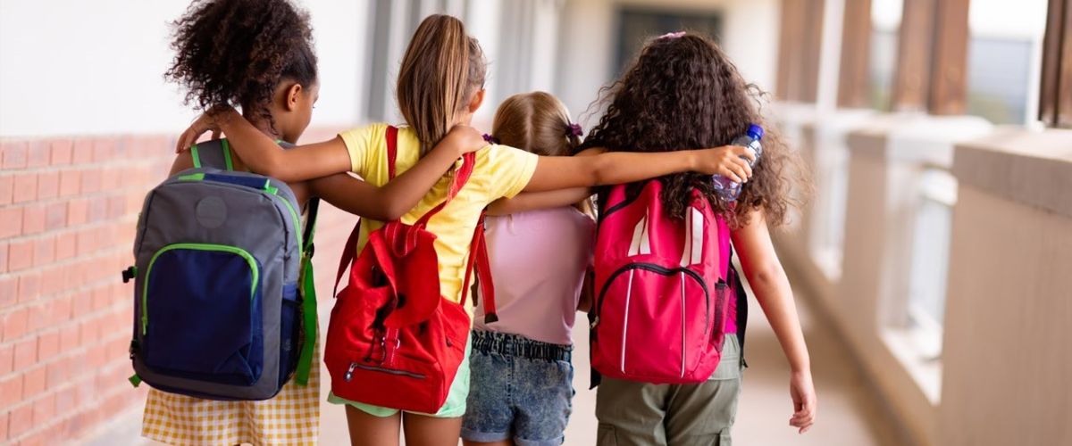 four girls arm in arm walking down a hallway with backs to the camera