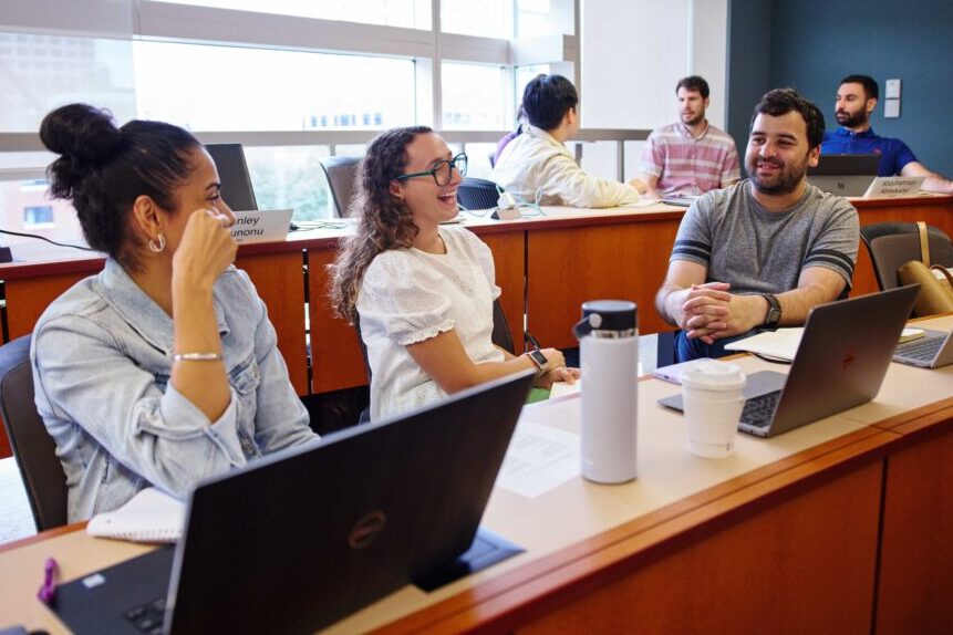 three students sitting in a classroom, engaging and laughing