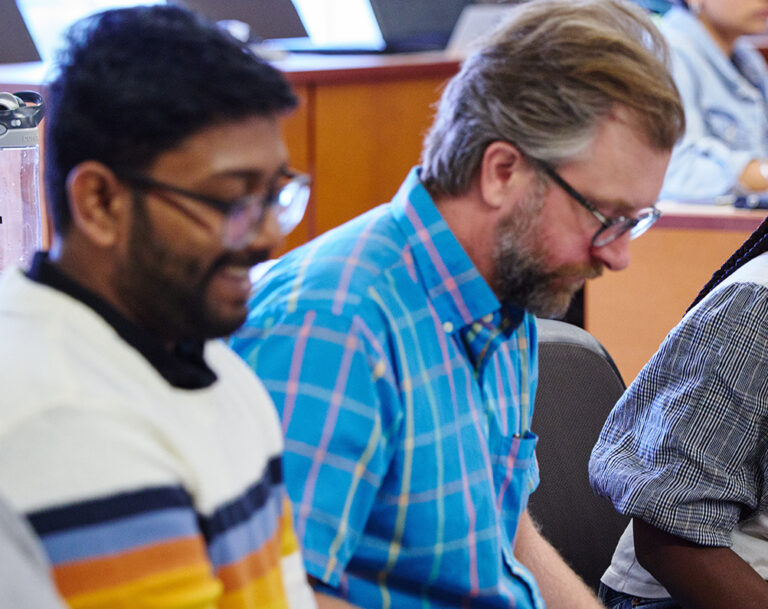 Woman sits in classroom engaging with three other male students.