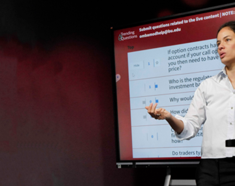 Woman professor stands in a studio in front of a screen teaching an online class.