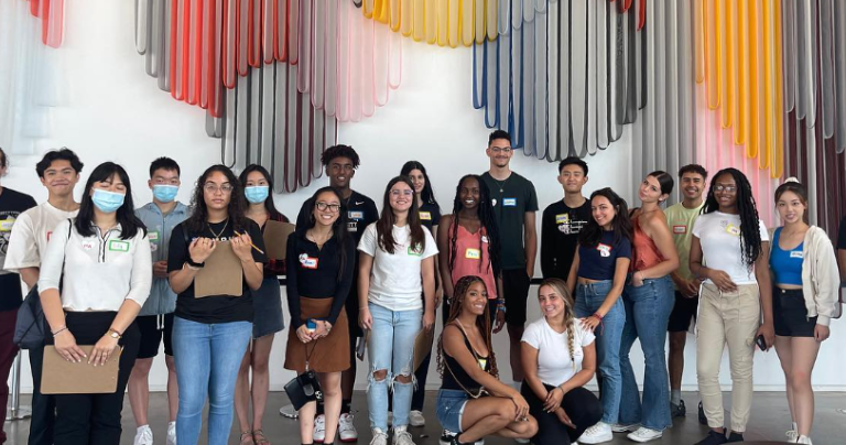 Group of students posed for a photo in front of a colorful statement wall.