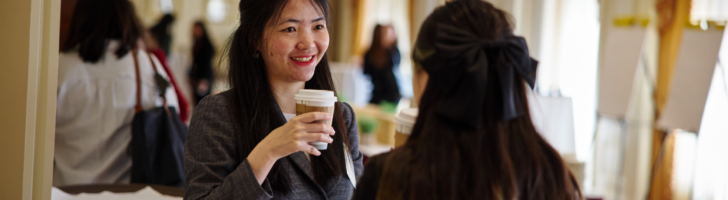 two women student stand at round table and chat