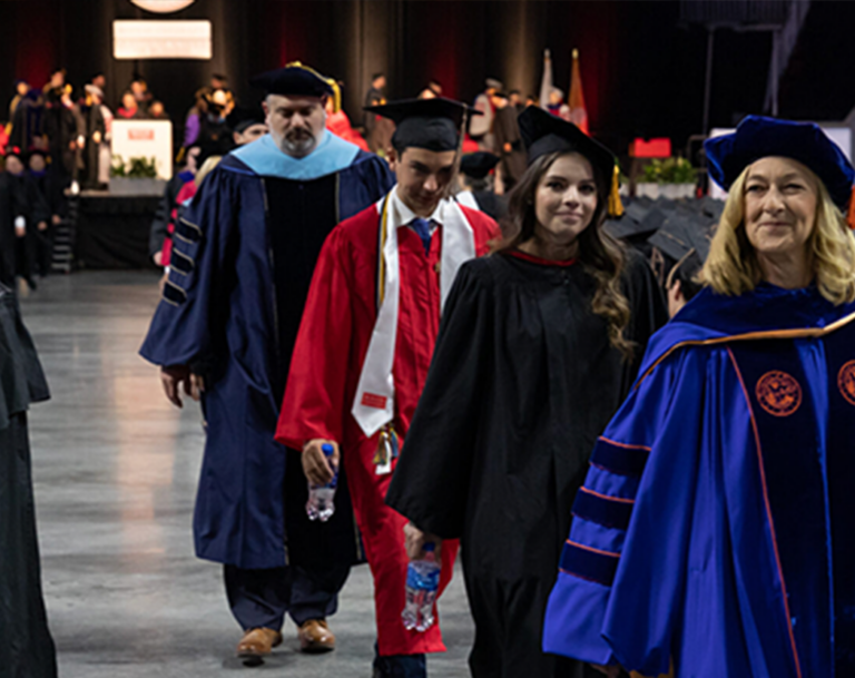 Dean Fournier leading a line of students across the floor at commencement
